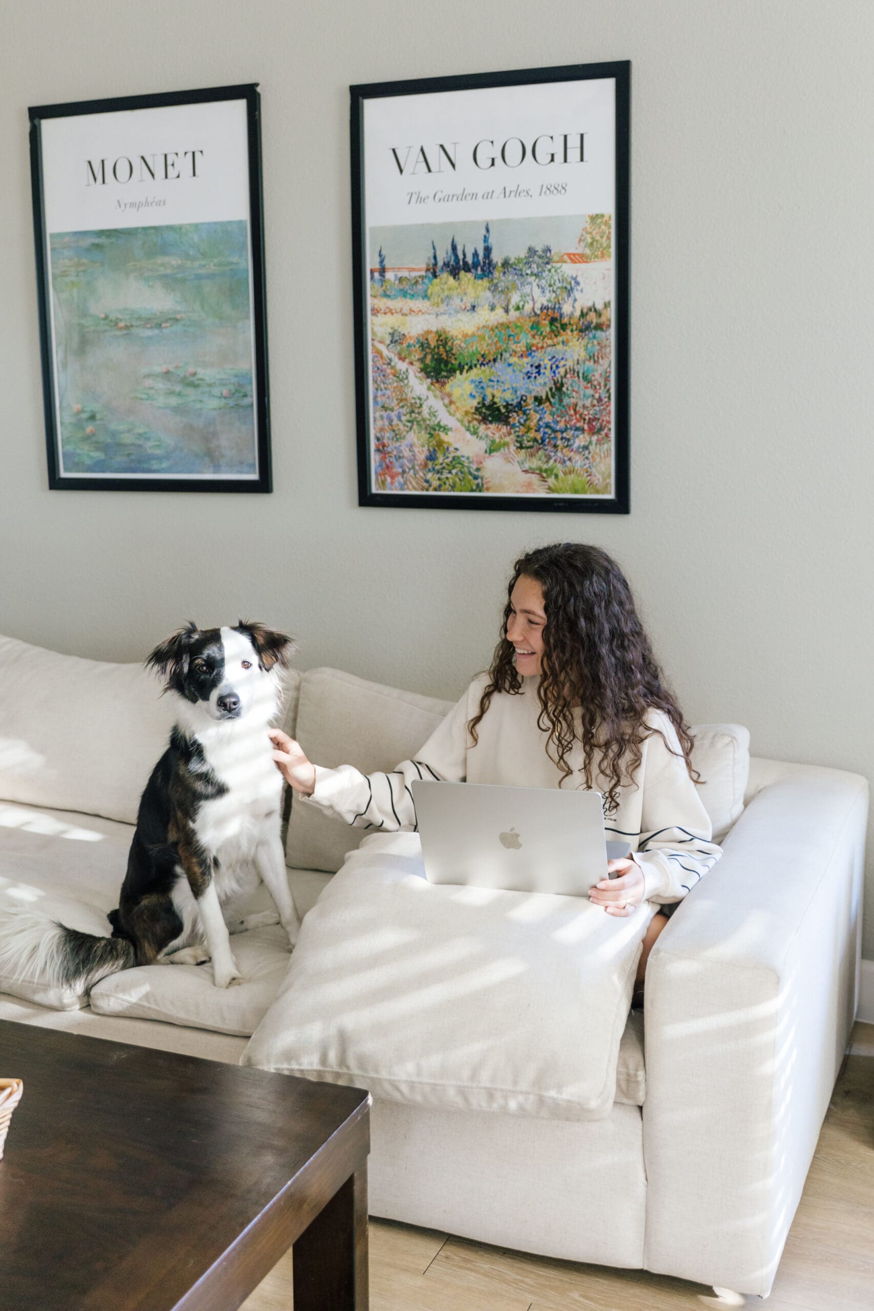 Woman sitting on a couch petting her dog while working from home on her laptop